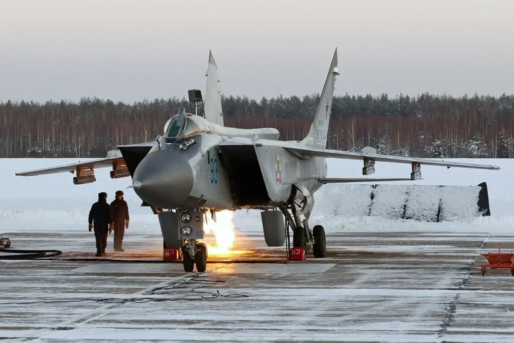 Interceptor MiG-31 de las Fuerzas Aeroespaciales rusas en una base aérea ártica con los motores encendidos, rodeado de nieve y bosque boreal.