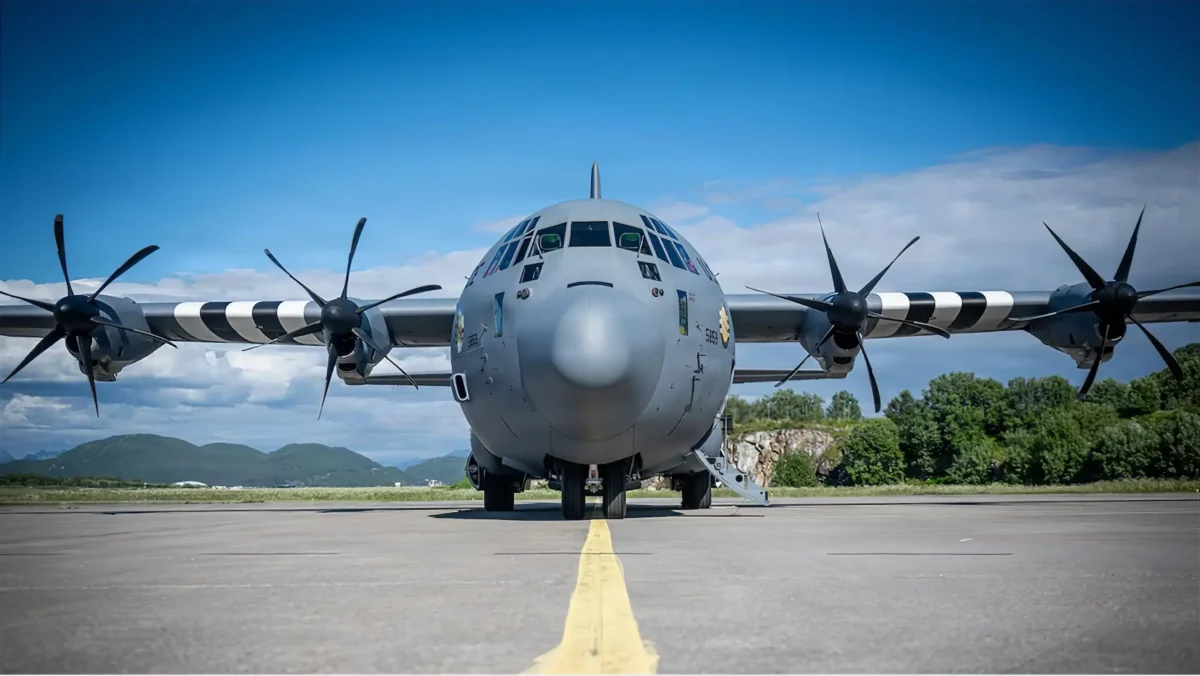 Avión de transporte militar C-130J Super Hercules de la Fuerza Aérea de EE. UU. estacionado de frente en la pista de la base aérea de Bodø, Noruega, bajo un cielo azul.