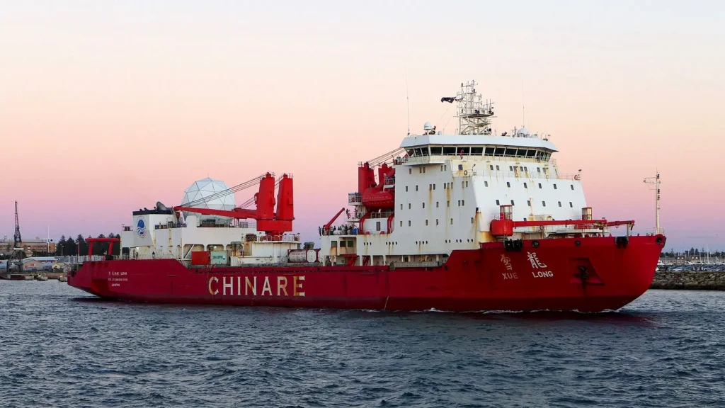 El rompehielos chino Xue Long navegando en el puerto de Fremantle, Australia, con su casco rojo característico y grúas de cubierta visibles.