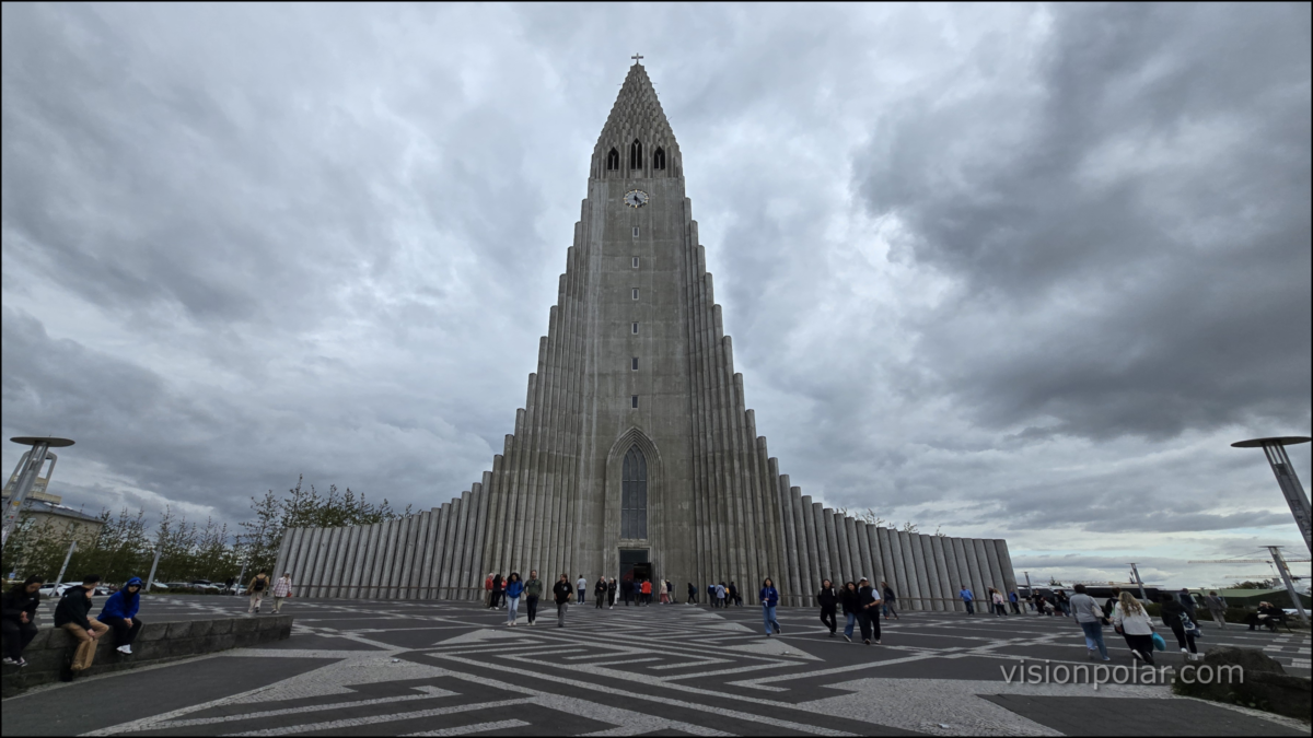 Iglesia Hallgrímskirkja en el centro de Reikiavik, Islandia, bajo un cielo nublado, con personas caminando por la plaza.