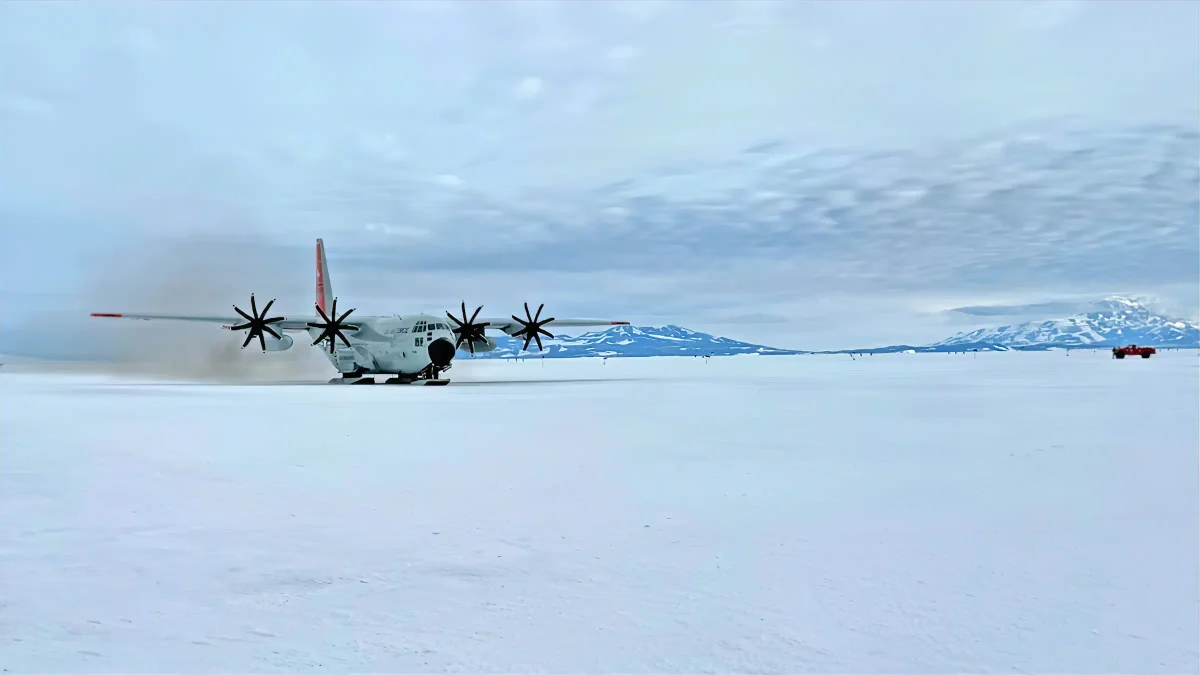 Un avión LC-130 Skibird de la Guardia Nacional Aérea de Nueva York aterriza sobre la nieve en la Estación McMurdo, Antártida, con montañas nevadas de fondo.