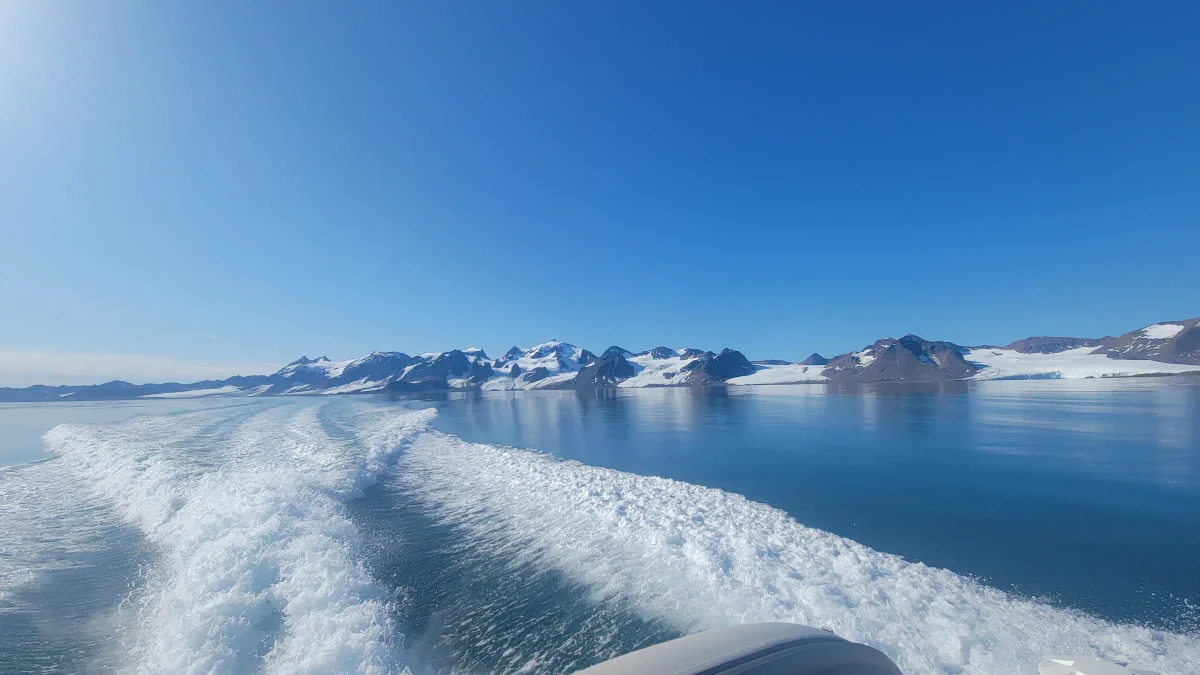Estela de una embarcación navegando por las aguas azules del fiordo Kongsfjorden en Svalbard, con montañas nevadas y glaciares de fondo.