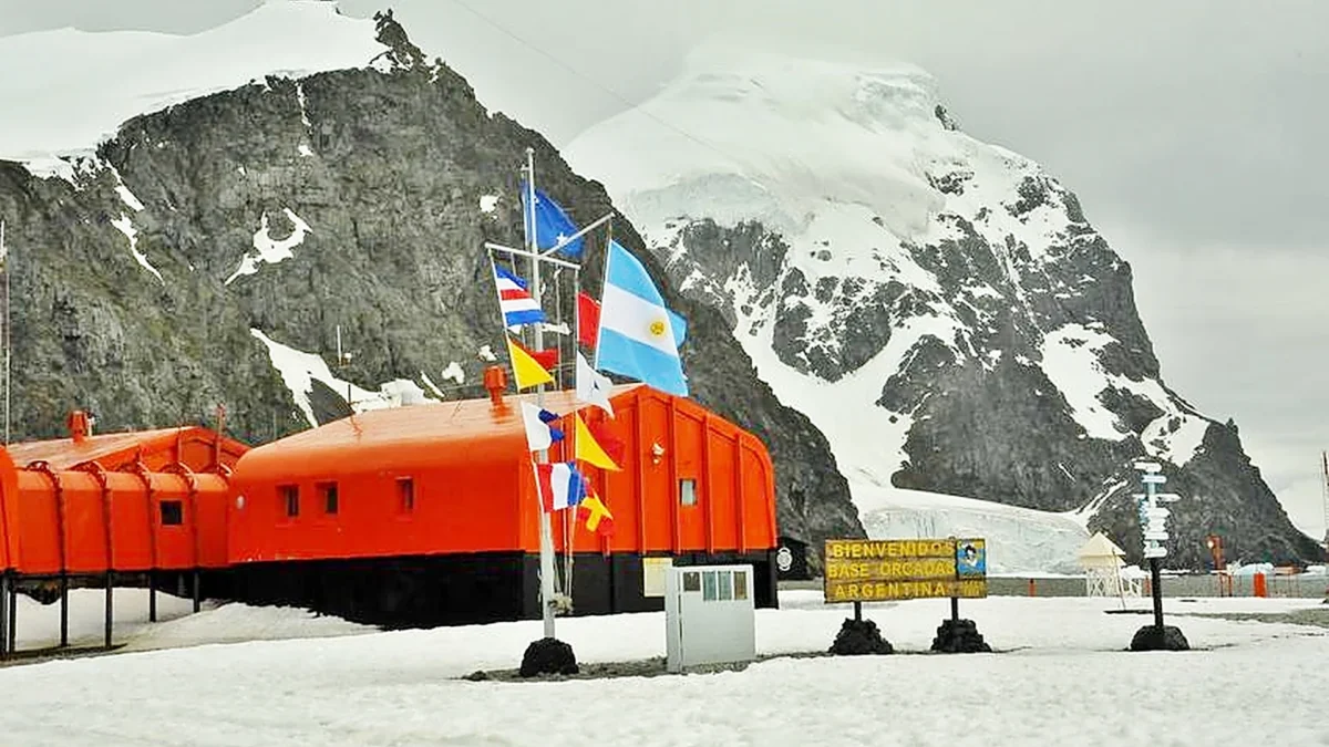 Edificios naranjas de la Base Orcadas con la bandera argentina y el macizo nevado de la isla Laurie, en la Antártida Argentina.