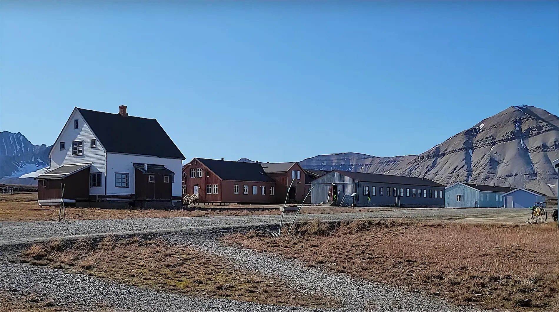 Edificios de madera blancos, rojos y grises de la comunidad científica de Ny-Ålesund, en Svalbard, con una montaña rocosa al fondo y tundra en primer plano.